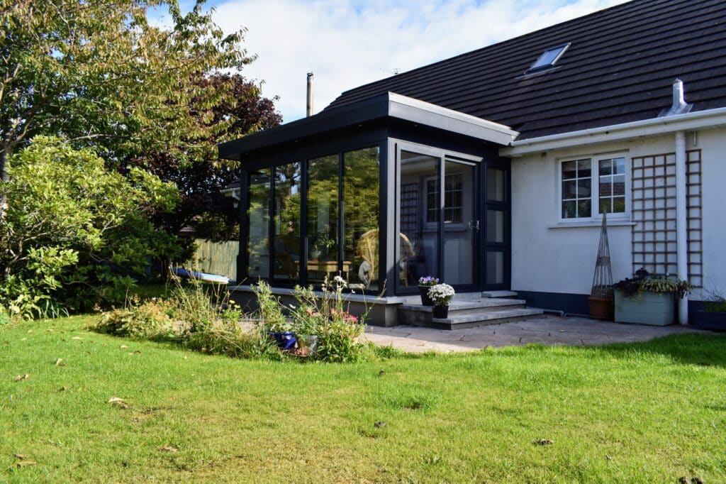 Flat roof pod sunroom on a bungalow in Ballynahinch, Northern Ireland, featuring insulated walls, warm roof and uPVC sliding doors by Budget Designer HomeWorks.